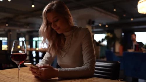 Joven mujer bonita y sonriente sentada en el restaurante con vino tinto y escribiendo un mensaje