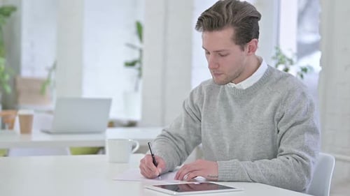 Hardworking Creative Young Man doing Paperwork in Loft Office