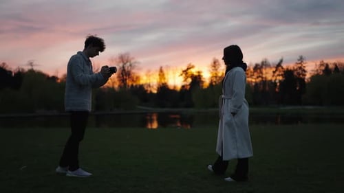 Young Man Photographing Woman in Park at Sunset