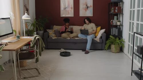 Couple Relaxing as Robot Vacuum Cleans Home