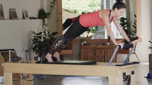 Fit senior caucasian woman stretching on reformer in pilates studio, unaltered, in slow motion