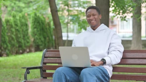 Smiling Man Using Laptop on Park Bench