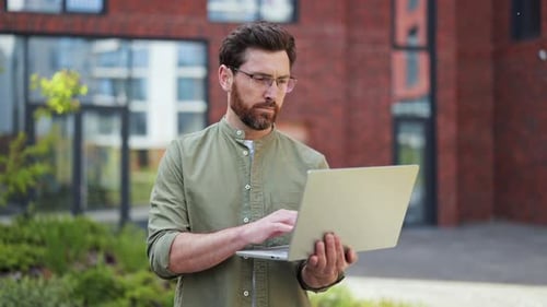 Handsome Businessman Working on Laptop Outdoors Near Office Building Joy Success and Confidence