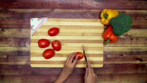 Eine Draufsicht auf das Schneiden der Tomaten von Hand, zwei große gelbe und rote Paprika und ein grüner Brokkoli