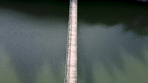Rural pedestrian suspension footbridge hanging over river stream aerial top down
