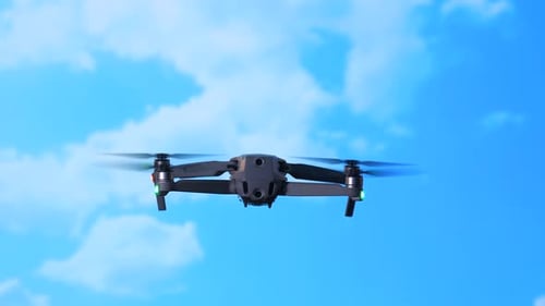 Drone Hovering in Blue Sky With White Clouds