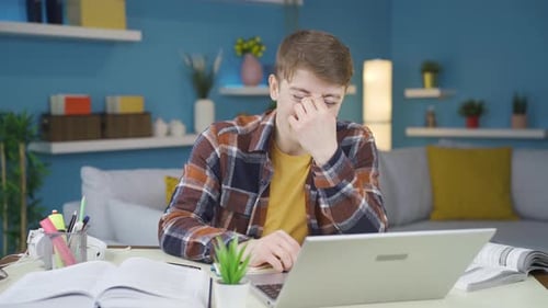 Young Adult Studying and Rubbing Eyes At Desk