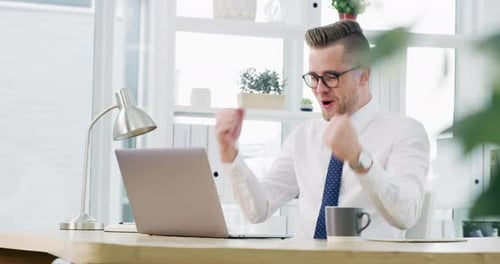 4k video footage of a young businessman cheering while working on a laptop in an office