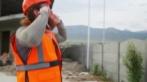 Um engenheiro civil barbudo com óculos escuros dança em um canteiro de obras, pula e comemora