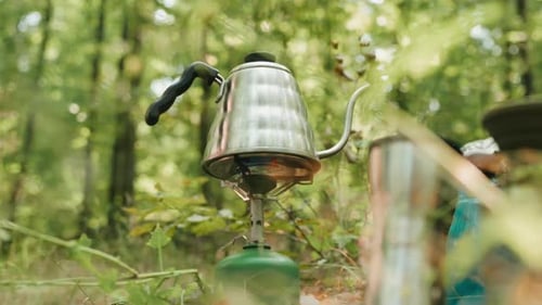 Shiny Kettle Boiling on Camping Stove in Forest