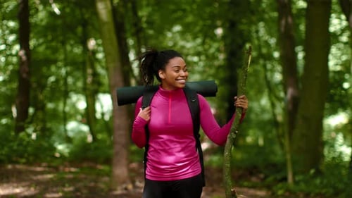 Woman Hiking in the Forest With a Yoga Mat and Stick During Daytime Outdoors