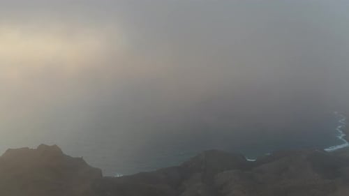 Dense early morning mist, aerial drone flying above mountain peaks landscape, pan reveals golden sun