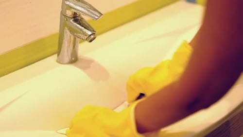 Mujer a cámara lenta haciendo tareas en el baño de su casa limpiando el lavabo y el grifo con detergente en aerosol