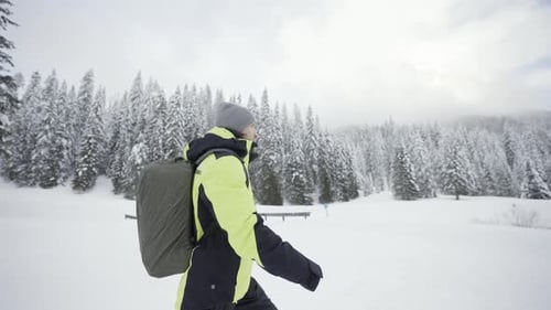 Man with Backpack Walks in the Snow Near the Forest