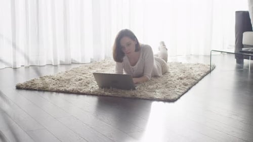 Woman Works on Laptop While Lying on Carpet