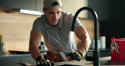 Young man repairing sink in modern kitchen