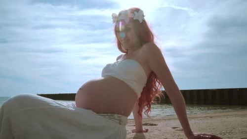 Jovem grávida feliz em uma praia ensolarada sorrindo com a barriga nua