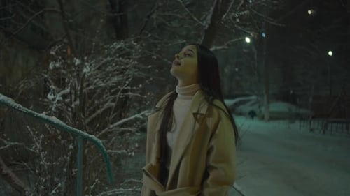 Girl Catching Snowflakes with Her Mouth on City Street at Night
