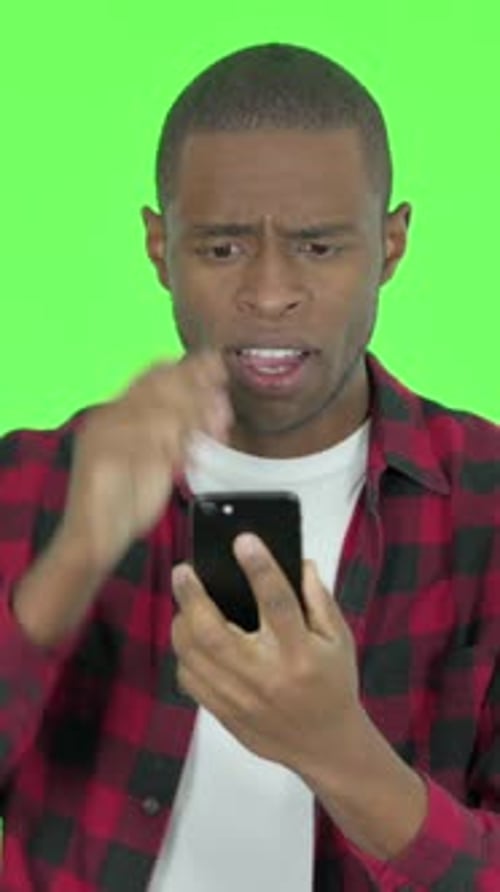African Man with Loss on Phone on Green Background, Vertical Video