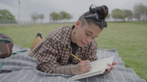 College Girl Lying on Green Lawn in Park and Writing in Copybook