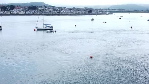 Aerial view small motorboat travelling Seaside town river Conwy harbour marina tracking left