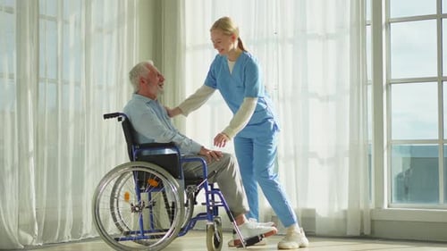 Kind Healthcare Worker Talking with Senior Man in Wheelchair