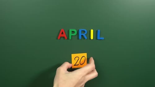 Hand sticking a sticker 20 April calendar day on school board. 20 date of April. Twentieth day