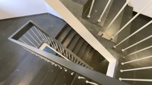 empty stairwell with white banister and dark stone steps in a circle below
