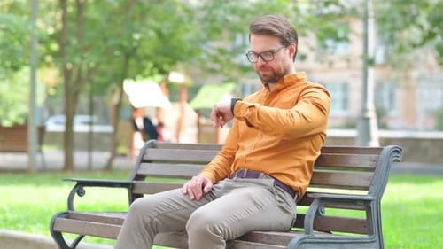 Man Checks Smartwatch While Sitting on Bench