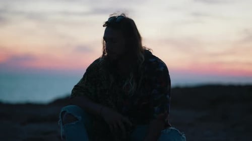 Man Sits at Dusk Using Phone by Ocean