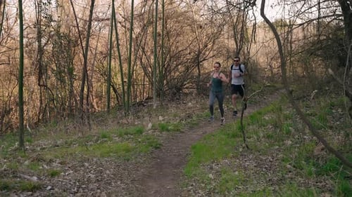 Smiling trail running couple jogs on dirt trail chasing each other through lush forest in slow