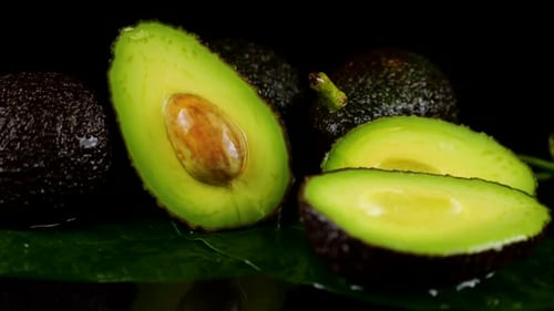 Drops of water fall on avocado fruits with leaves on a black background. Raw Fruits, healthy food.
