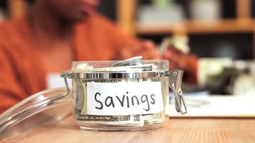 Woman Putting Money in Savings Jar Close Up