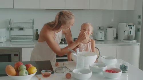 Loving Cheerful Mother and Little Daughter Having Fun While Cooking Pastries Sprinkling Sugar Powder
