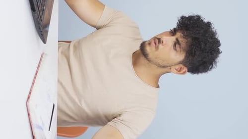 Vertical video of Man working on laptop throws files angrily.