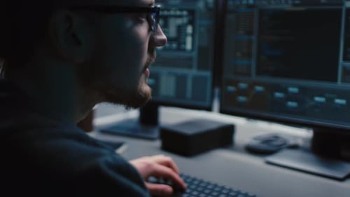 Portrait of IT Specialist Wearing Glasses Works on Personal Computer with Screens Showing Software