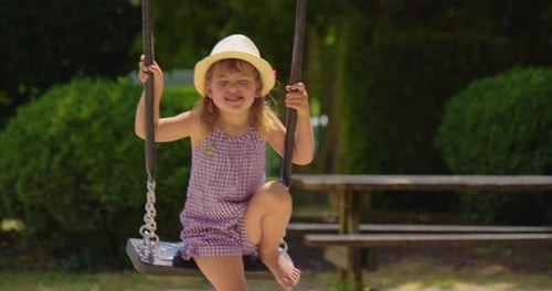Petite fille se balançant sur une balançoire, concept de rêve de parc d'attractions, heureuse fille au chapeau se balançant sur une balançoire