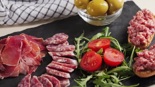 Assiette à goûter : tartare de bœuf, tomates cerises, olives vertes et saucisse de fuet, jamon. Snack au vin.