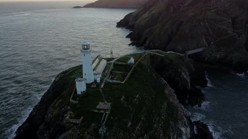 South Stack lighthouse aerial descending view of rugged island mountains during golden hour sunrise