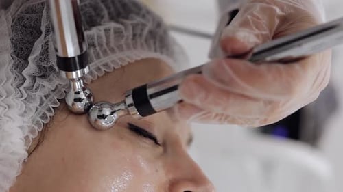 Middleaged Woman Receiving Micro Currents Facial Temples Skin Treatment From Beautician in Clinic