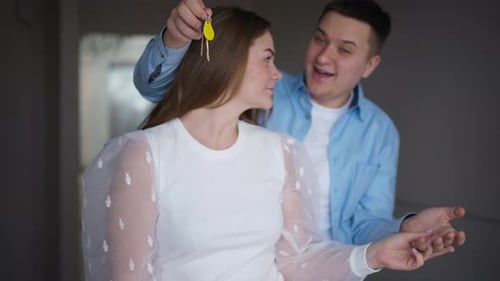 Surprised Beautiful Woman Standing with Happy Handsome Man in New Flat As Boyfriend Passing Key to