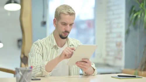 Young Man Browsing Internet on Tablet in Office