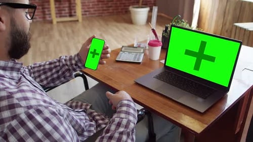 Man in Wheelchair Holds Green Screen Phone at Desk
