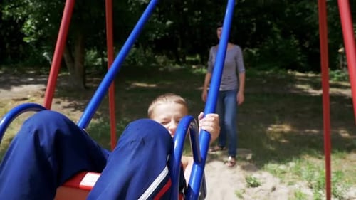 Mother Swinging Her Happy Child Boy on a Street Swing at Playground in Slow Motion