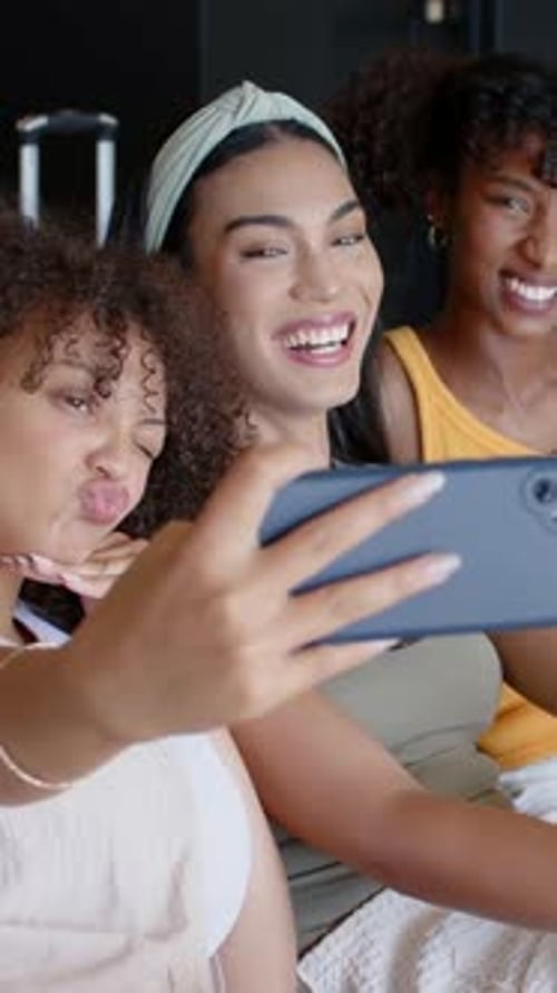 Estendendo o telefone azul, três mulheres tirando selfie, revisando fotos no lounge, mulher do meio apontando