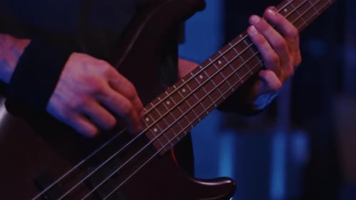 Musician Skillfully Playing Bass Guitar on Stage Amidst Vibrant Blue Lights