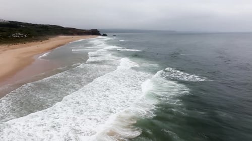 Breaking Waves Crashing Onto a Sandy Beach with Cliffs in the Background