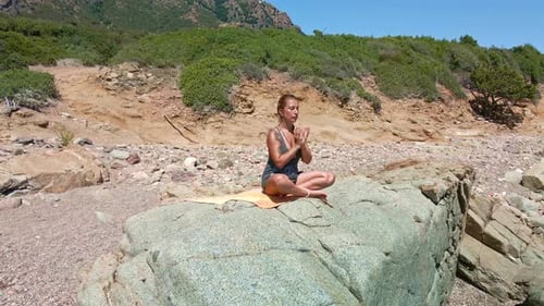 Beautiful Woman Meditating With Eyes Closed And Sitting On A Rock By The Sea In Sardinia, Italy - ae