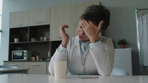 Stressed Doctor Massages Temples, Drinks from Paper Cup