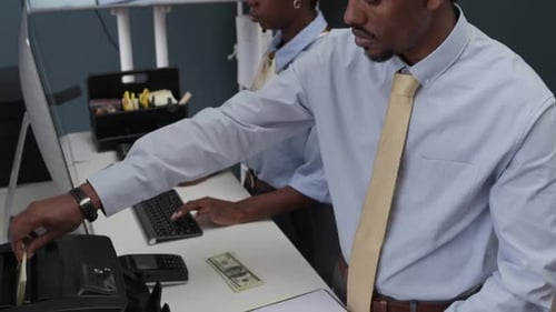 Bank Employee Counting Cash in Machine while Colleague Working on Computer